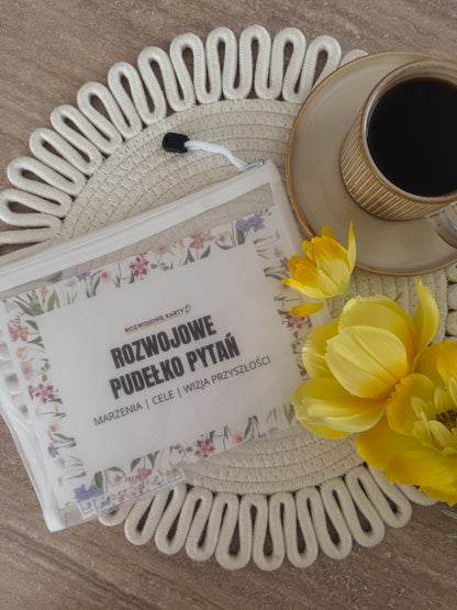 Pudełko z kartami do gry Poznajmy się - marzenia, cele i wizja przyszłości na stole obok kawy i żółtych kwiatów